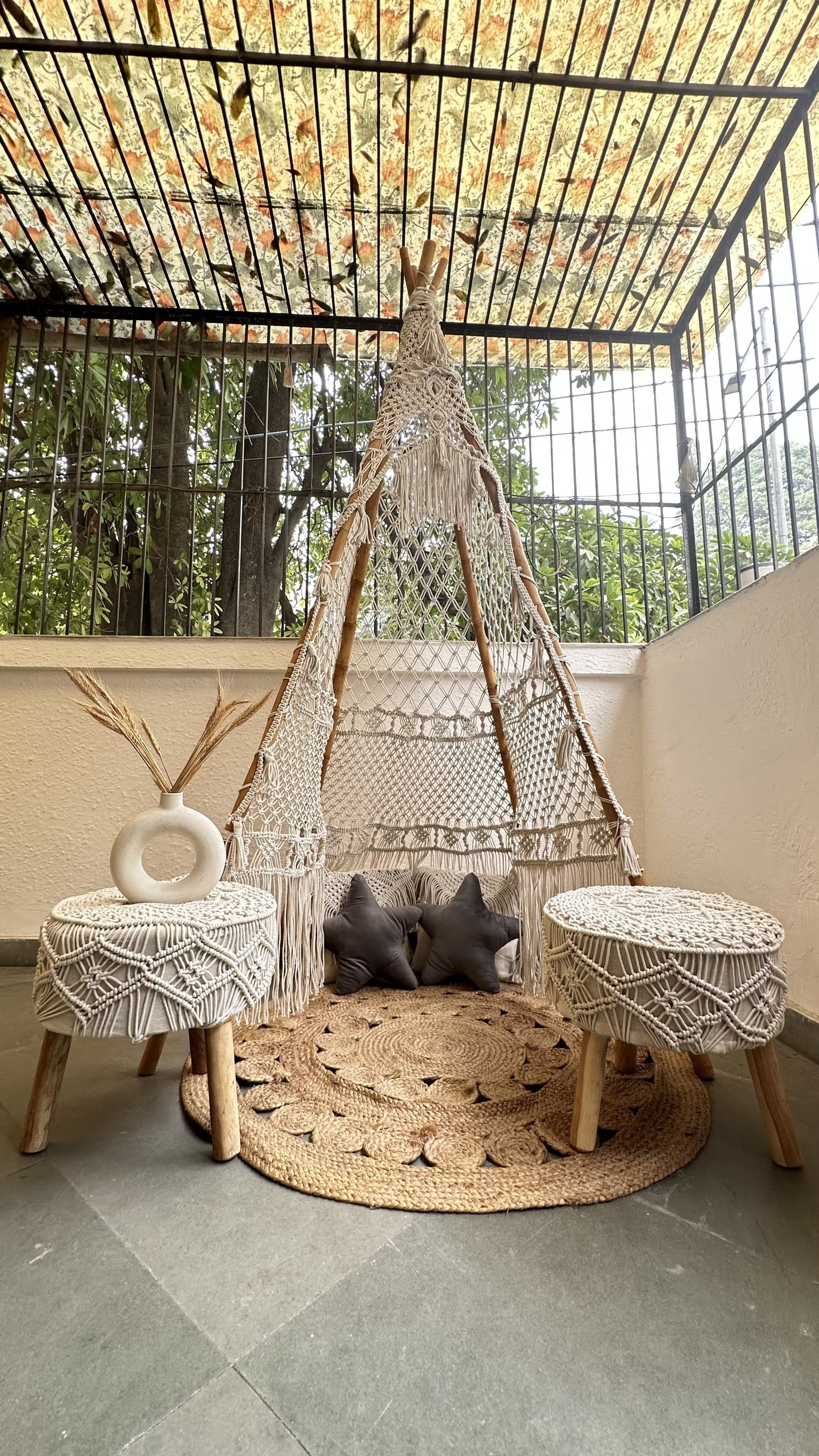 Handmade macrame teepee in white color with a pair of ottoman placed in an outdoor setting.
