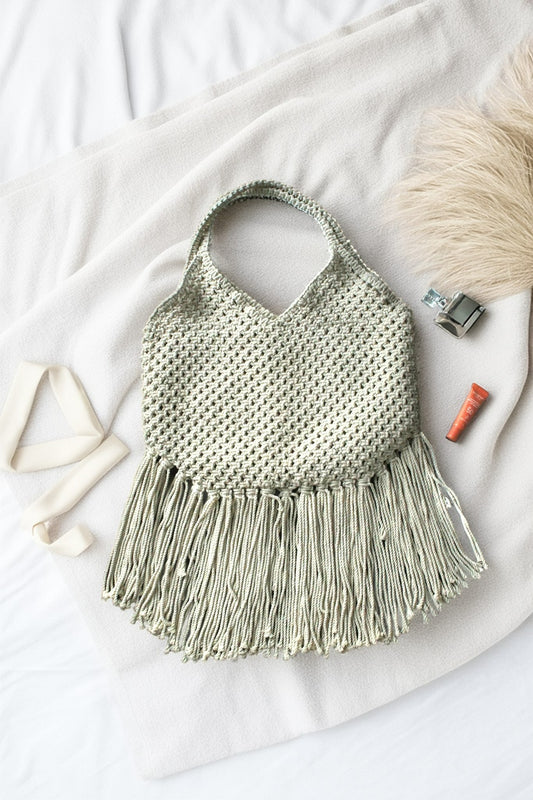 Photo of macrame bag in off white color with long fringes placed at a white background.