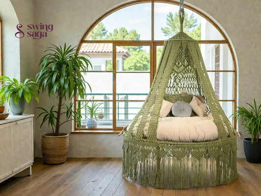 Green macrame hanging chair in a room with large windows and a plant.