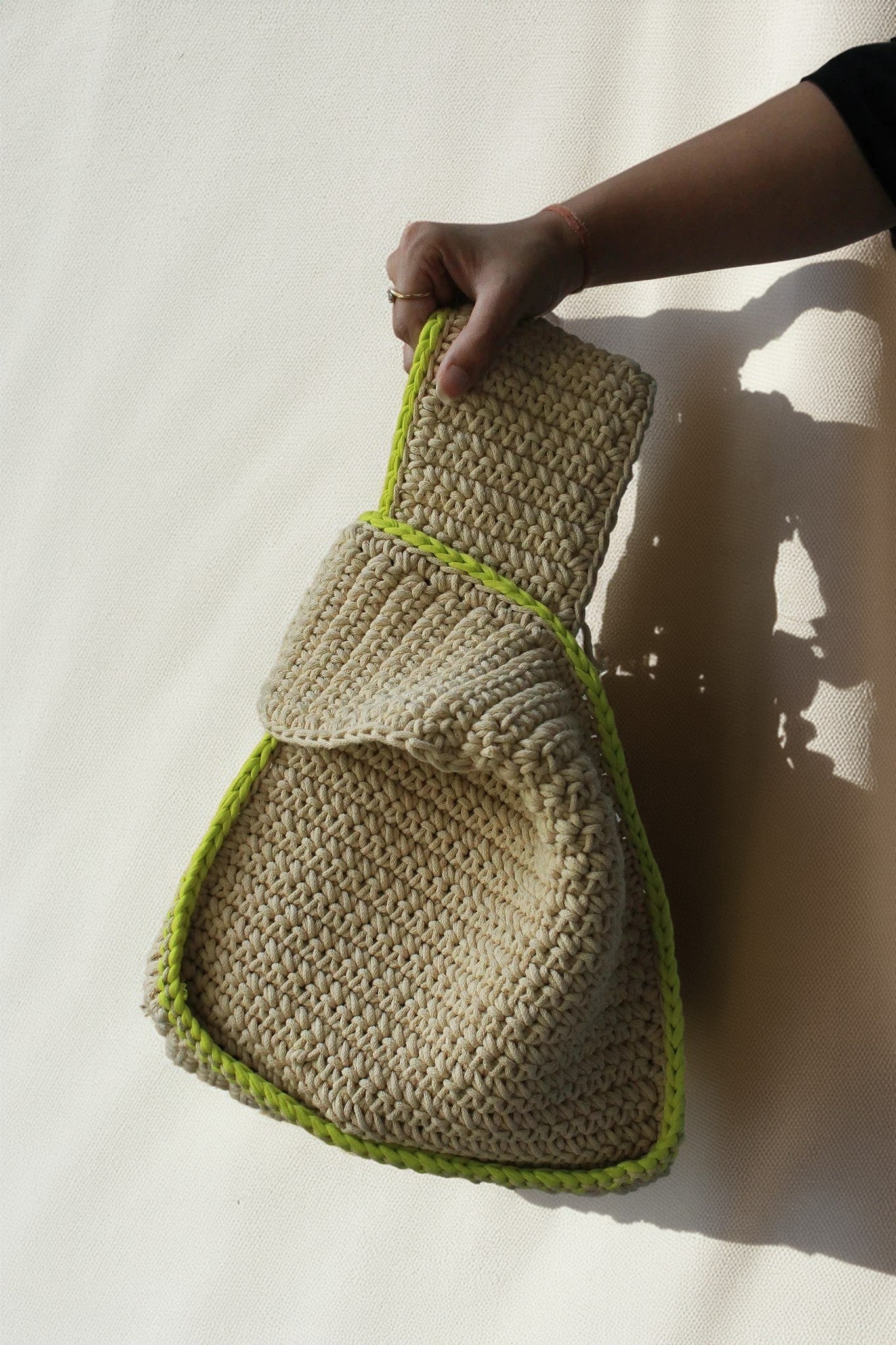 a girl holding a modern sling bag in beige color with green border.