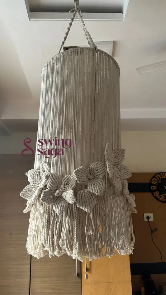 A cream colored macrame handcrafted chandlier hanging with flower attached, with ring on top.