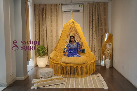 Woman sitting inside a yellow woven chair in a room with curtains and decor.