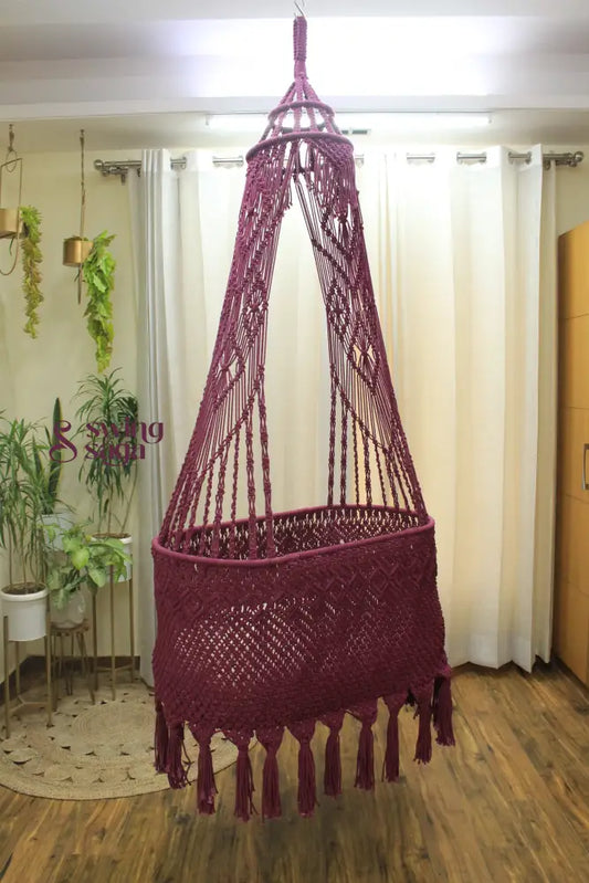 brown colored handcrafted macrame baby bassinet hanging in an indoor setting.