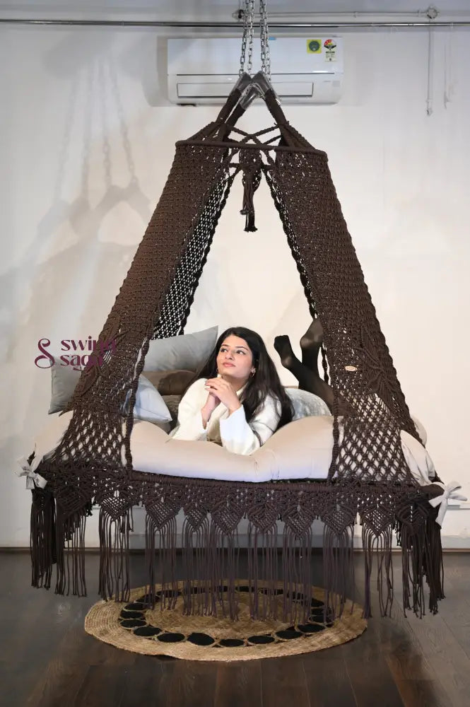 Macrame hanging square bed swing with jute rug in indoor setting.