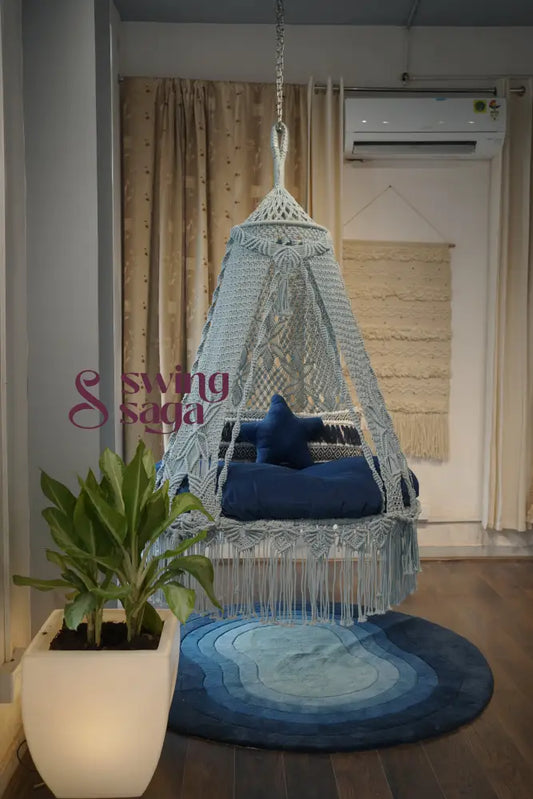 Hanging chair with a blue cushion on a wooden floor next to a plant and rug.