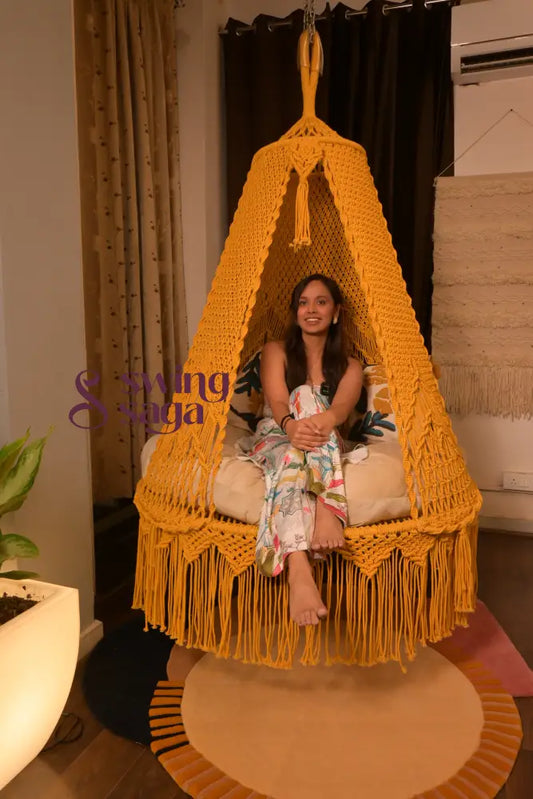Woman sitting in a yellow fringed chair in a room with a lamp and plant.