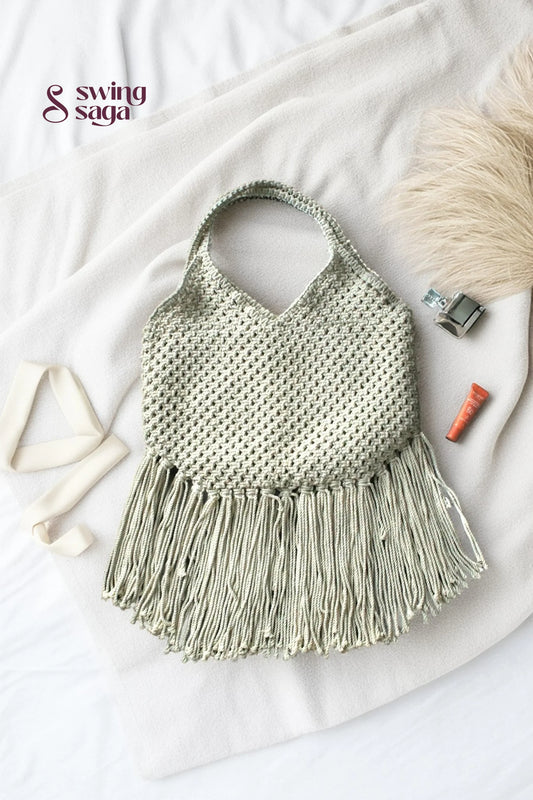 Photo of macrame bag in off white color with long fringes placed at a white background.