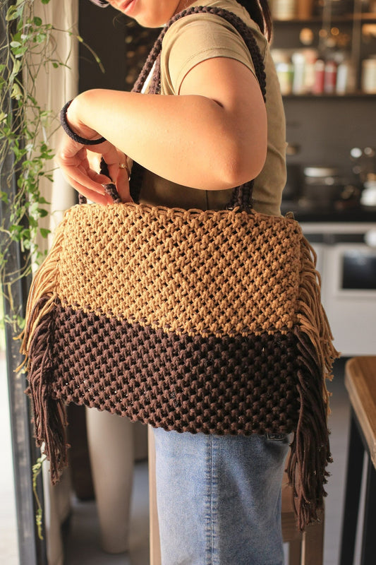 A girl holding macrame bag in brown and dark brown color. it has fringes from every side.