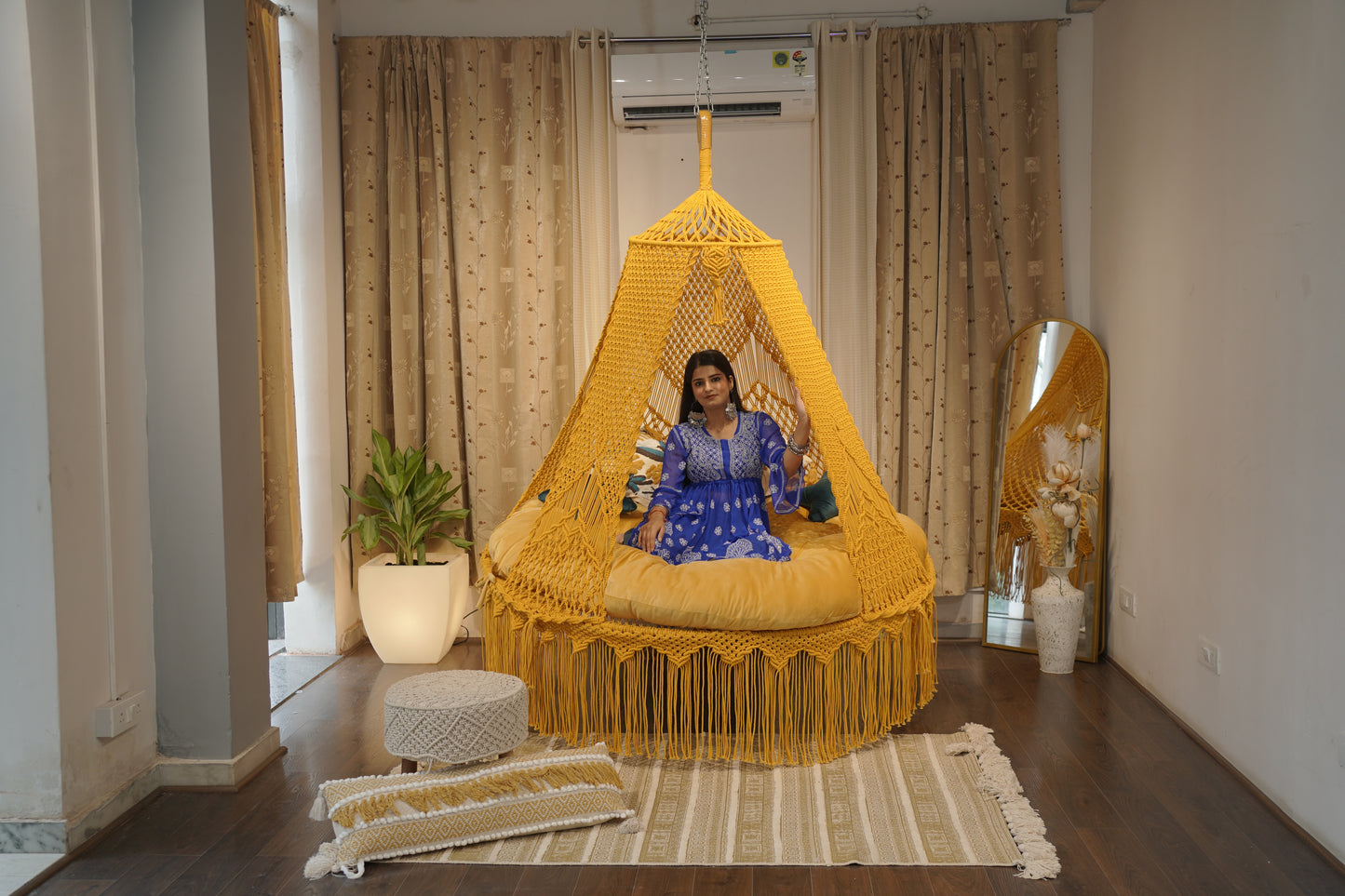 Woman sitting inside a yellow woven chair in a room with curtains and decor.