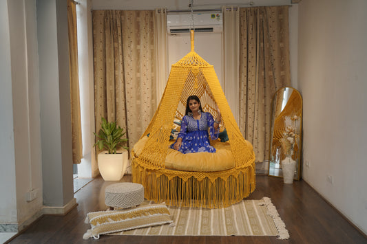 Woman sitting inside a yellow woven chair in a room with curtains and decor.