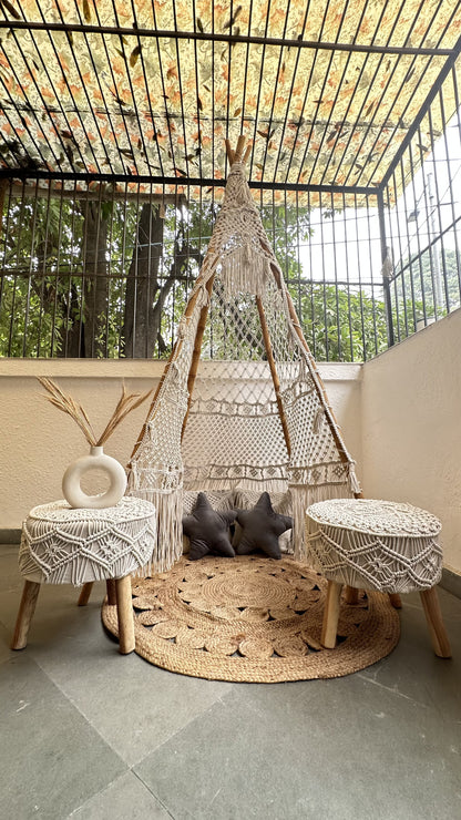 Handmade macrame teepee in white color with a pair of ottoman placed in an outdoor setting.