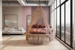 Hanging macrame bed with pink cushions in a room with pink walls and large windows.