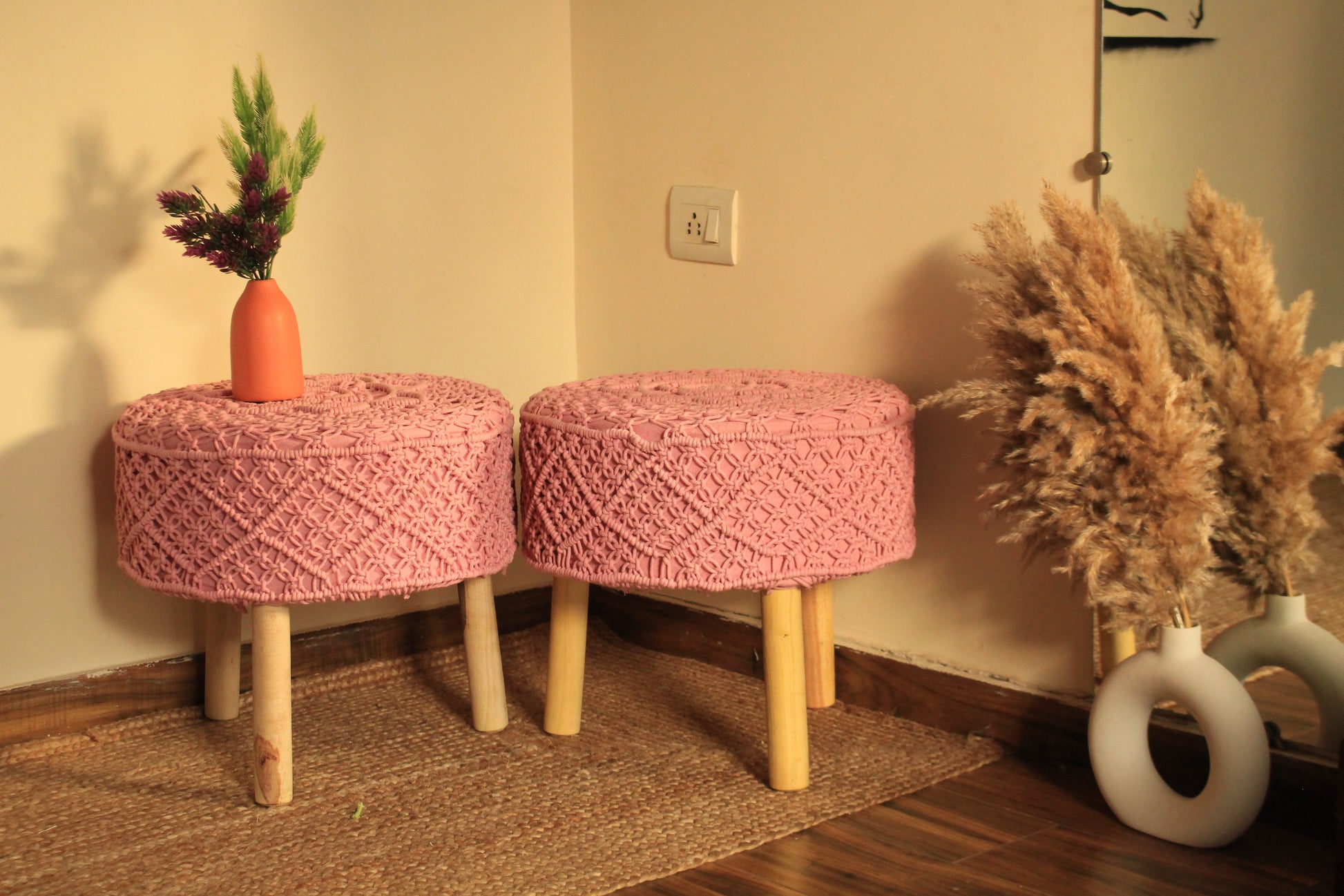 Two pink woven stools with wooden legs in a room setting.