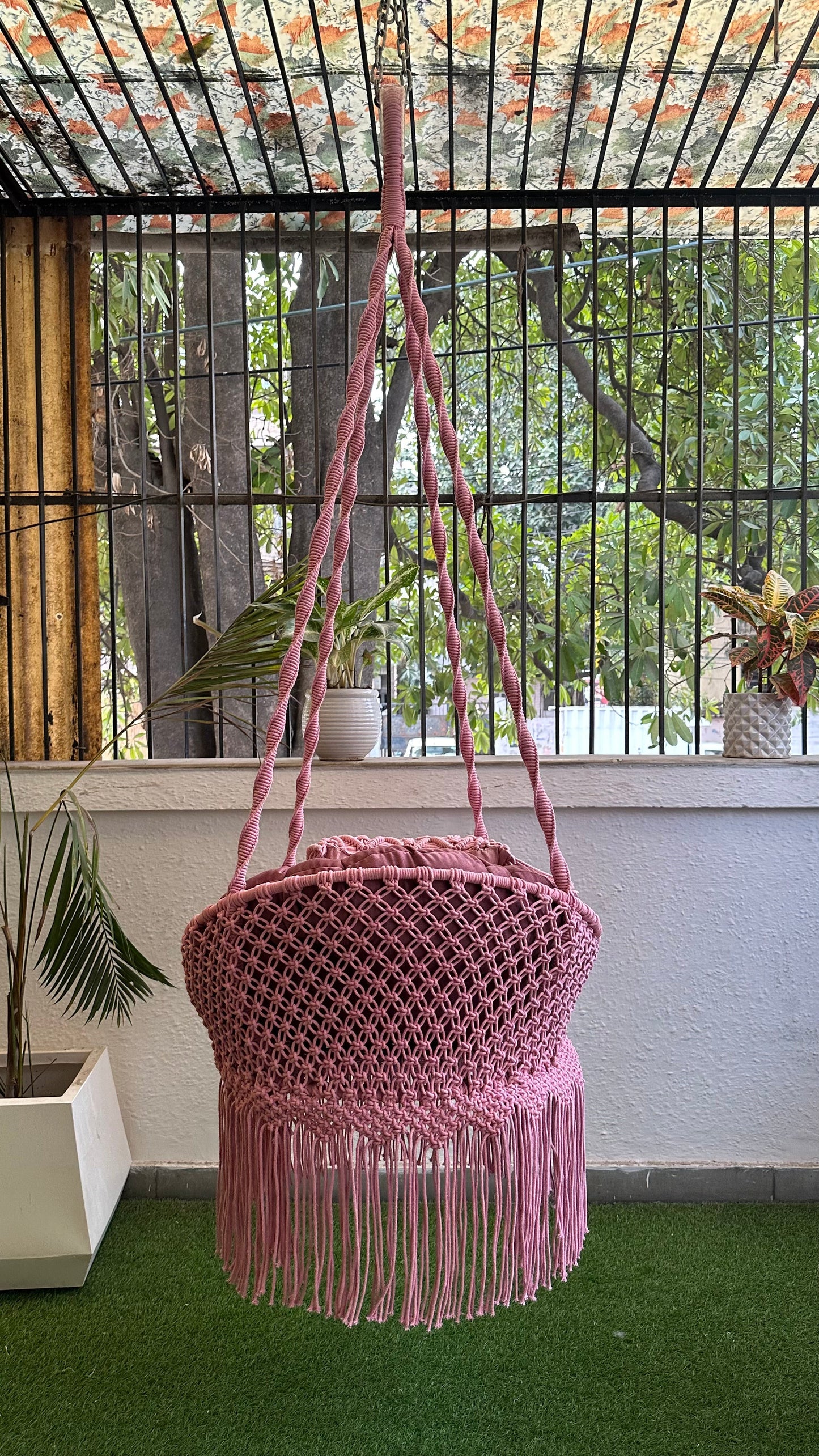 Handmade pink macrame chair swing hanging in a cozy closed balcony