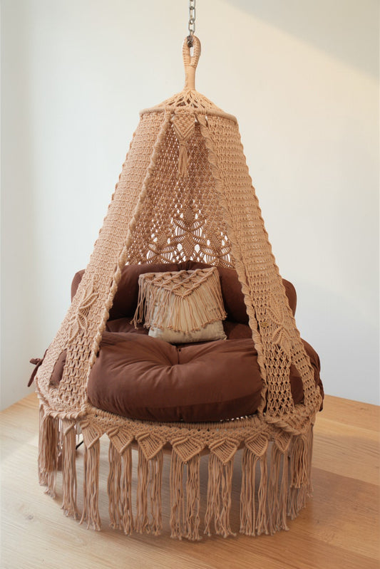 Hanging macrame chair with brown cushions on a wooden floor.