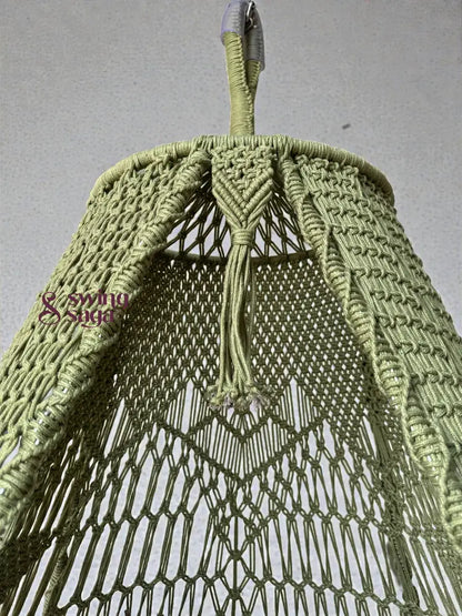 Close-up view of an olive green handcrafted macrame swing top, showing detailed knotting, braided hanging loop, and netted pattern against a neutral wall background.