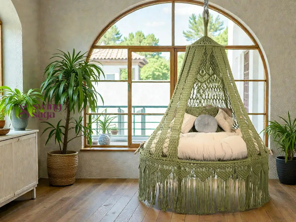 Green macrame hanging chair in a room with large windows and a plant.