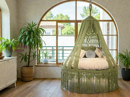 Green macrame hanging chair in a room with large windows and a plant.