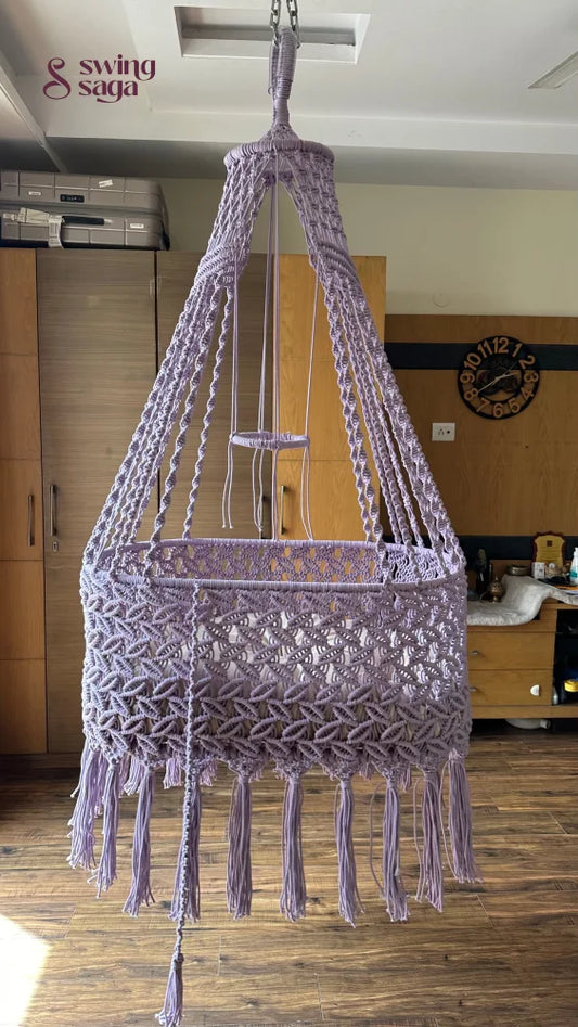 Macrame handcrafted baby bassinet in lavender color in a room setting. 