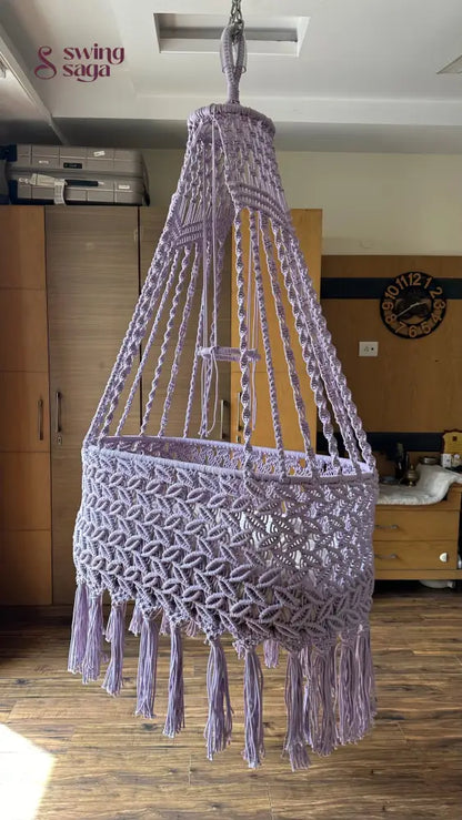 Lavender macrame baby bassinet hanging in a cozy nursery room, handcrafted cotton rope cradle for newborns.