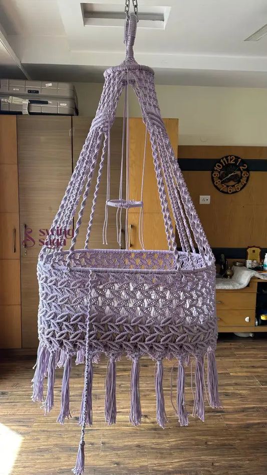 Macrame handcrafted baby bassinet in lavender color in a room setting. 