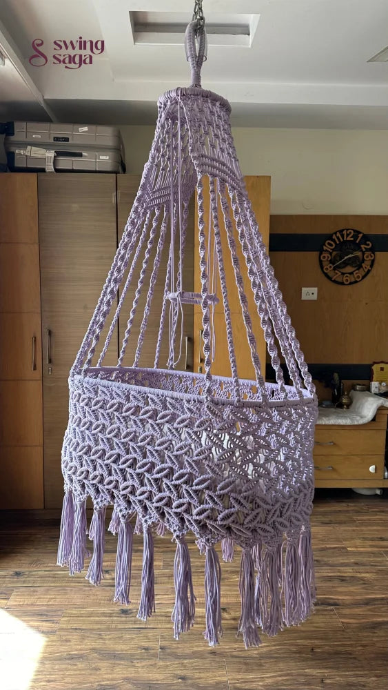 Lavender macrame baby bassinet hanging in a cozy nursery room, handcrafted cotton rope cradle for newborns.