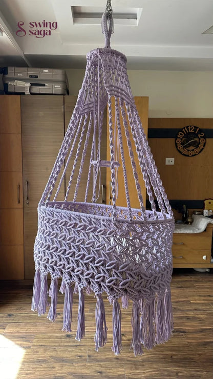 Lavender macrame baby bassinet hanging in a cozy nursery room, handcrafted cotton rope cradle for newborns.