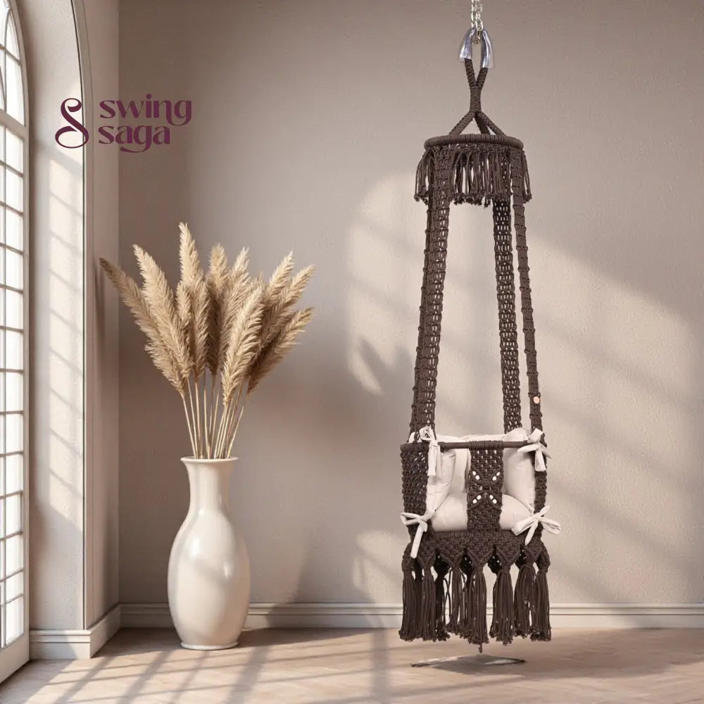 Brown baby swing with tassels in a room with a vase of pampas grass.
