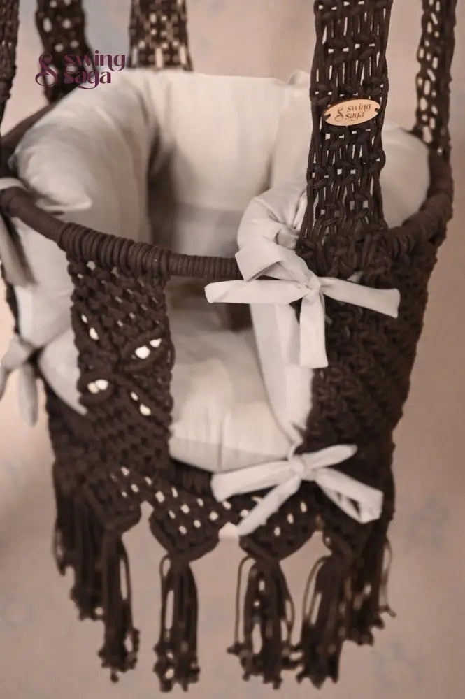 Brown baby swing with white ribbons on a neutral background