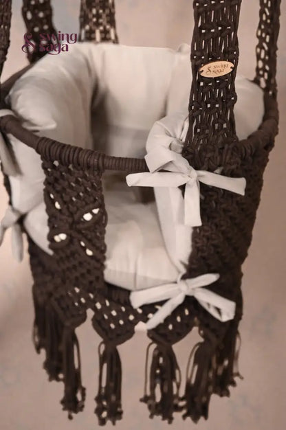 Brown baby swing with white ribbons on a neutral background