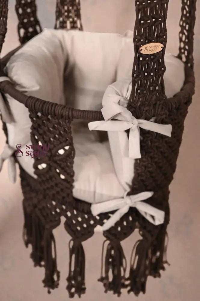 Brown baby swing with white ribbons on a neutral background