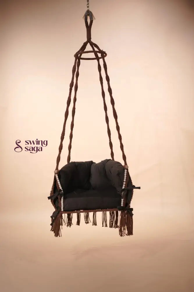 Hanging macrame chair swing with dark cushions against a beige background
