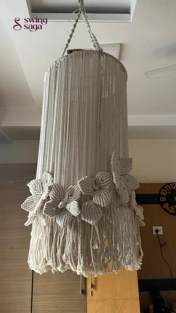 A cream colored macrame handcrafted chandlier hanging with flower attached, with ring on top.
