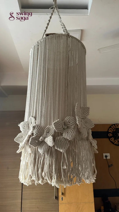 A cream colored macrame handcrafted chandlier hanging with flower attached, with ring on top.