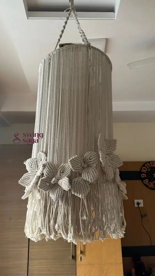 A cream colored macrame handcrafted chandlier hanging with flower attached, with ring on top.