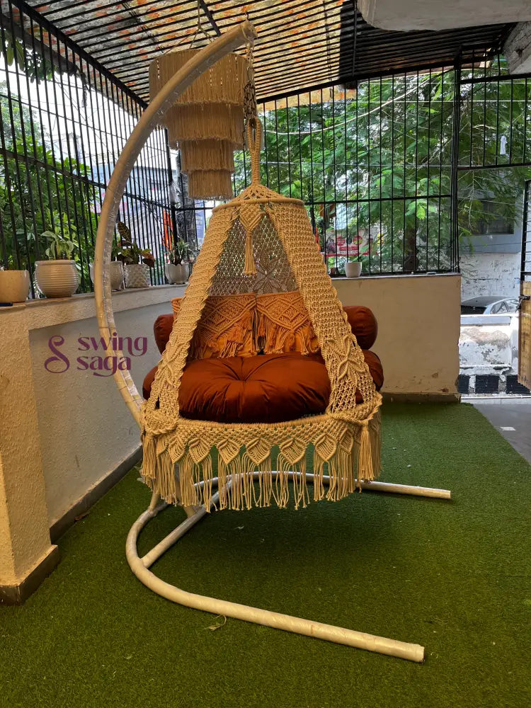 macrame swing is attached with a Metal white stand on a faux grass
