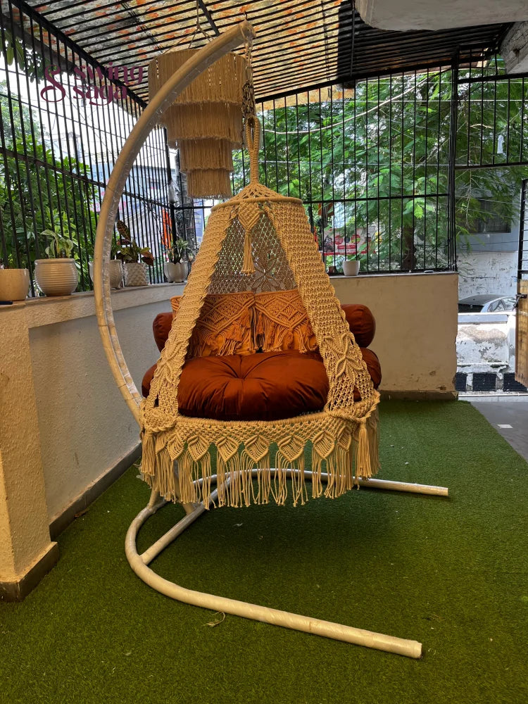 macrame swing is attached with a Metal white stand on a faux grass