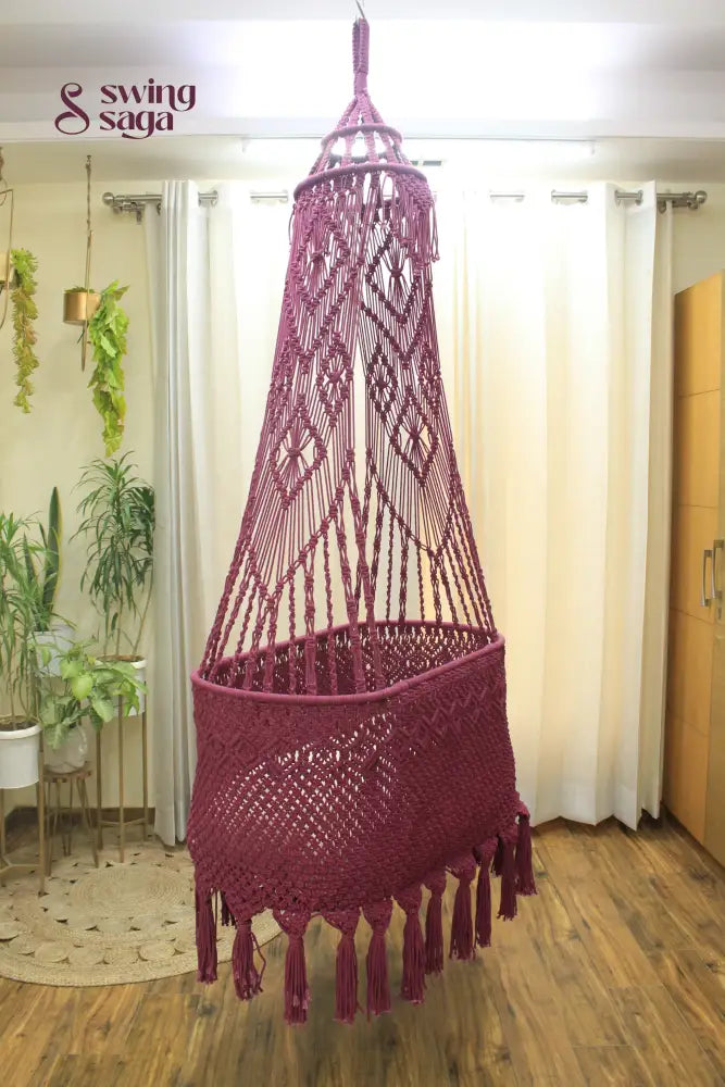 Macrame handcrafted Brown colored baby bassinet hanging in a room with planters.