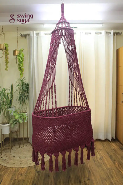 brown colored handcrafted macrame baby bassinet hanging in an indoor setting.