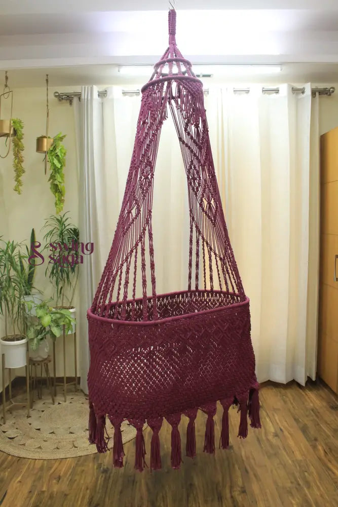 brown colored handcrafted macrame baby bassinet hanging in an indoor setting.