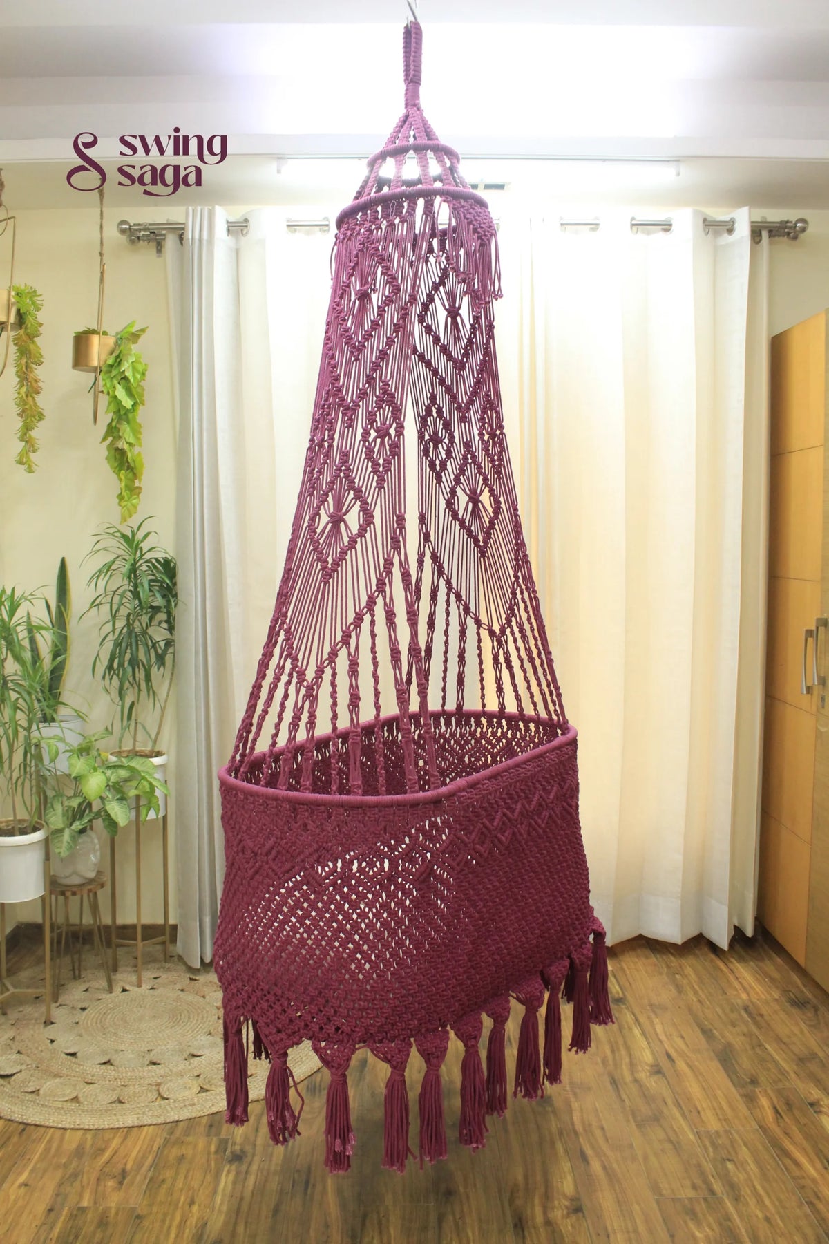 Macrame handcrafted Brown colored baby bassinet hanging in a room with planters.