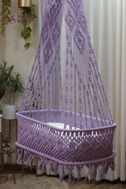 Lavender macrame baby bassinet swing hanging from ceiling in a modern home.