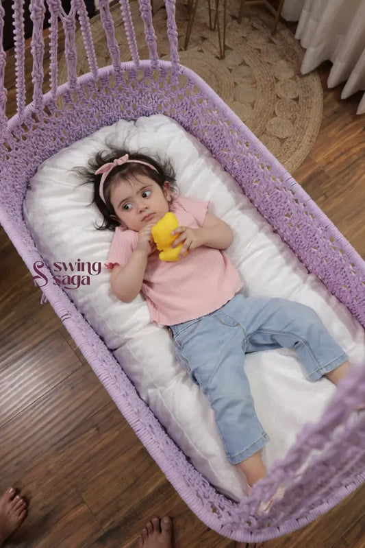 Baby girl lying in a lavender macrame hanging cradle swing with cushion in a cozy indoor home setting