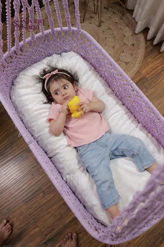 Baby girl lying in a lavender macrame hanging cradle swing with cushion in a cozy indoor home setting