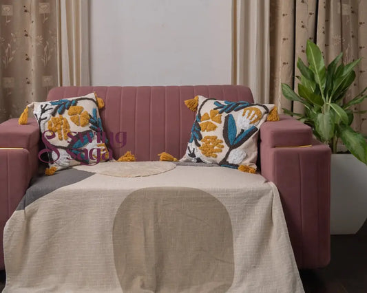 Pink sofa with decorative pillows and a blanket in a room with curtains and a plant.