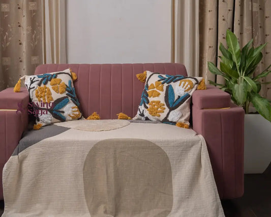 Pink sofa with decorative pillows and a blanket in a room with curtains and a plant.