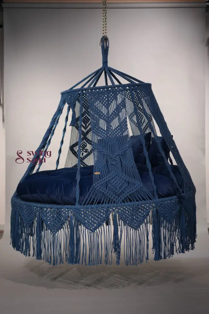 Blue macrame hammock chair with fringe on a plain background