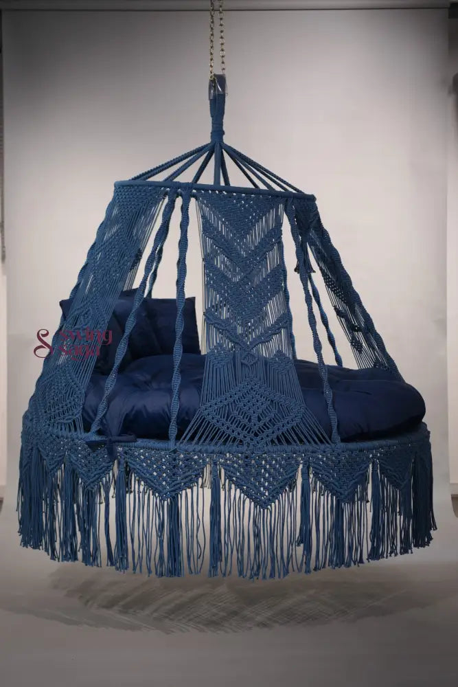 Blue macrame hanging chair with cushions on a plain background