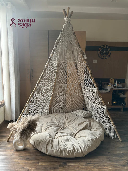 Macrame handmade teepee in white color with white mattress placed on a wooden floor.