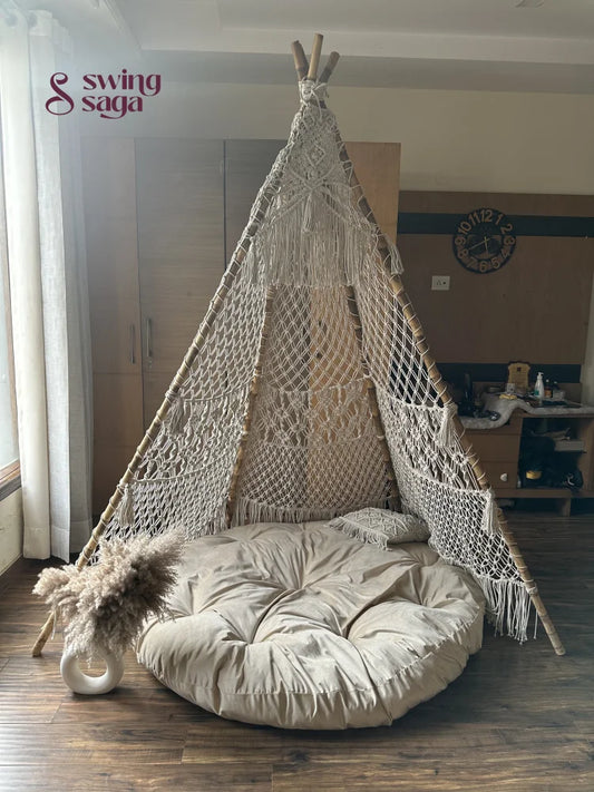 Macrame handmade teepee in white color with white mattress placed on a wooden floor.